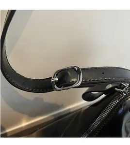 Detail of adjustable black glossy leather strap with silver oval metal buckle on tote bag