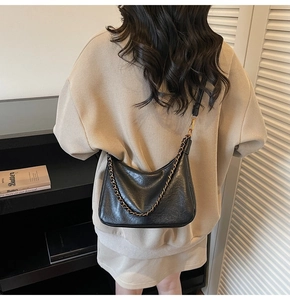 Rear view of a model wearing a black pleated leather tote bag with vintage gold chains