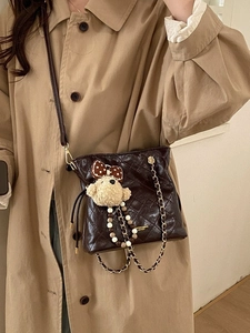 Quilted dark brown bucket bag with plush bear charm worn with a stylish khaki trench coat