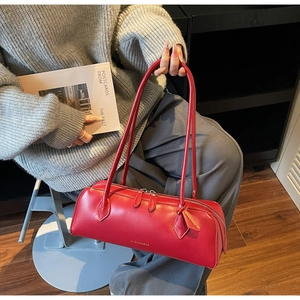 Detail of red French baguette handbag with long handles held by model in casual setting