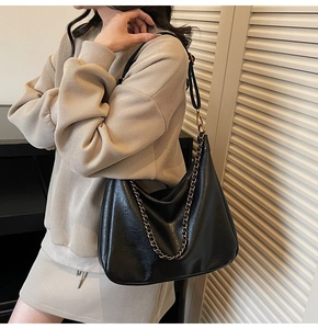 Detail of black hobo bag with pebble leather texture and bold gold chain strap