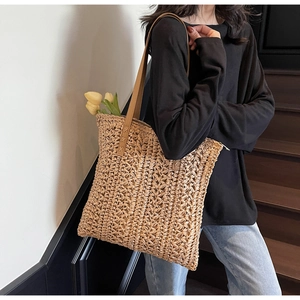 Detail of woven straw tote bag with brown faux leather straps and reinforced stitching