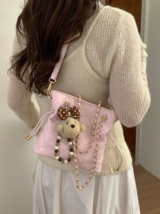 Pink quilted bucket bag with gold chain strap and cute bear charm shown on a model