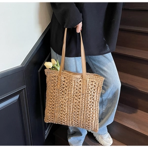 Detail of hand-woven straw tote bag with brown faux leather handles and secure cross stitching