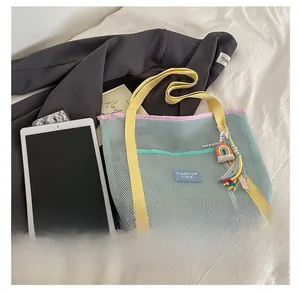 Détail du sac cabas en maille multicolore avec breloque arc-en-ciel sur lit blanc