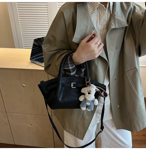 Detail of black leather bucket bag featuring a decorative buckle and a cute bear plush pendant