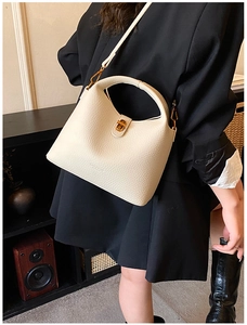 Détail du sac seau en cuir grainé crème avec fermoir doré sur une veste noire
