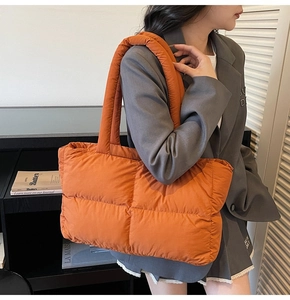 Close-up of a large orange quilted puffer tote bag worn on a shoulder for daily styling