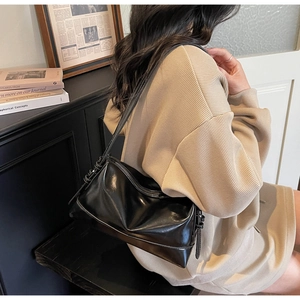 Detail of minimalist black glossy leather shoulder bag with zipper closure on model