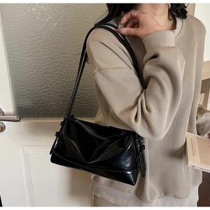 Detail of a high-gloss black baguette bag with pleat design worn by a model in beige