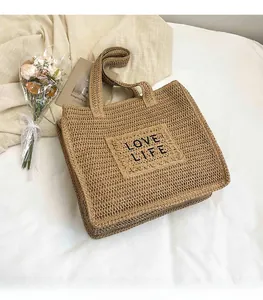 Détail du sac cabas en paille tissée avec broderie Love Life noire sur tissu beige