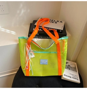 Détail du sac cabas en filet néon avec sangles orange et breloque arc-en-ciel à franges