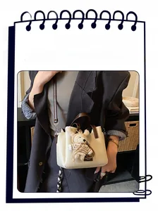 Detail of cream pebbled leather bucket bag with brown handle and striped bear charm