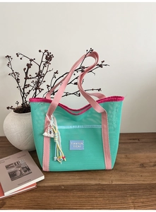 Détail d'un sac cabas en maille vert menthe avec anses roses et pendentif à pompon arc-en-ciel