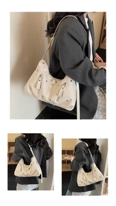 Detail of cream white faux leather hobo bag with silver rivets and decorative zippers