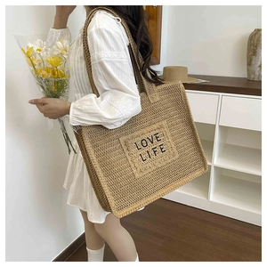 Détail de la broderie LOVE LIFE et texture tissée sur un grand sac en paille