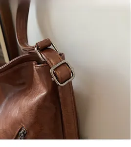 Close-up of smooth brown leather shoulder strap with adjustable metal buckle on bag