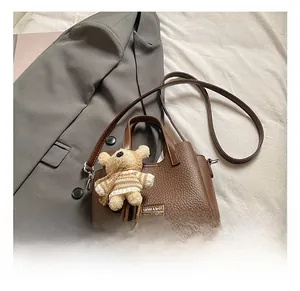 Macro detail of dark brown litchi grain leather handbag with silver hardware and bear charm