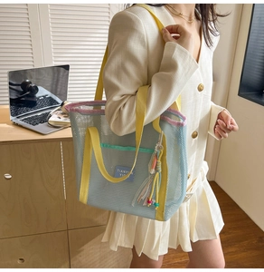 Détail du cabas en maille bleu clair avec anses jaunes porté par un mannequin en intérieur