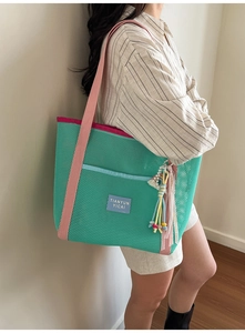Détail d'un grand sac cabas en filet vert avec poche bleue et sangle rose