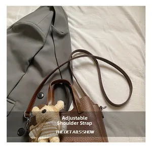Detail of brown lychee grain leather handbag featuring adjustable strap and bear charm