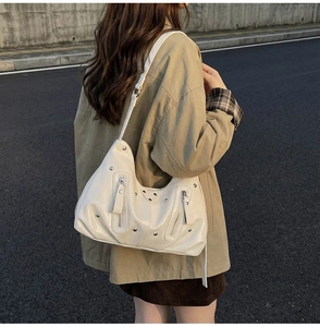 Detailed view of white high-gloss underarm bag with metal studs and decorative zippers