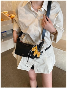 Détail d'un sac bandoulière minimaliste en cuir noir avec sangle et breloque jaune