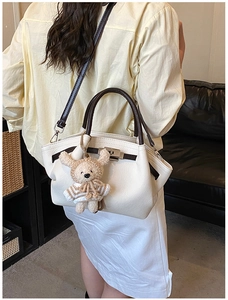 Detail of white lychee textured tote bag with dark brown handles and knit bear charm