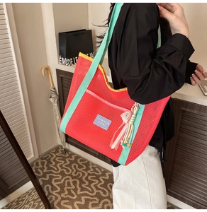Détail du sac cabas en maille rouge avec pendentif à pompon coloré et étiquette bleue