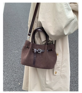 Detail of dark brown textured bucket bag featuring suede finish and metallic buckle strap