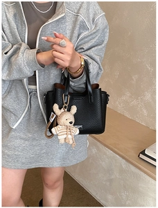 Detail of black lychee leather tote bag with white logo and cute plush bear charm