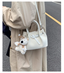 Detail of white woven bucket bag with cute plush bear pendant and textured pattern