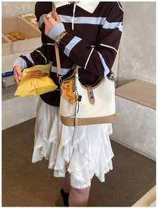 Detail view of cream and brown bucket bag with horse charm and metal lock on a model