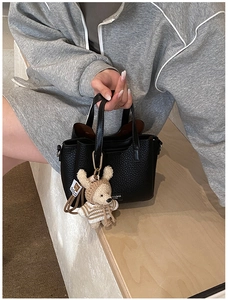 Close-up of black lychee grain leather handbag with a cute teddy bear charm detail
