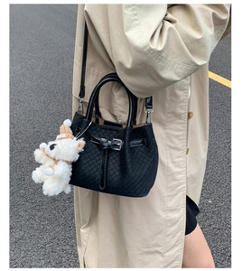 Detail of black woven crossbody bag with cute plush dog charm worn with a trench coat