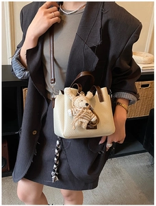 Close-up of cream textured leather handbag with contrast brown handles and a bear charm
