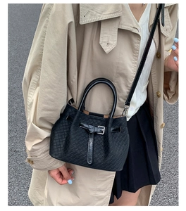 Detail of black woven leather bucket bag featuring a polished buckle and textured finish