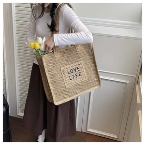 Détail du texte LOVE LIFE brodé sur un sac fourre-tout en paille beige de vacances