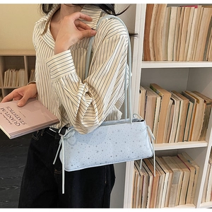 Détail du sac baguette bleu clair avec motifs étoiles argentées et nœuds décoratifs sur le côté