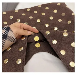 Detailed macro view of the gold magnetic closure on a brown suede studded tote bag