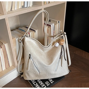 Close-up of cream textured leather bag with baseball charm and zip pocket details