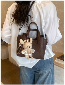 Detail view of dark brown pebbled leather tote bag with a cute bear charm accessory