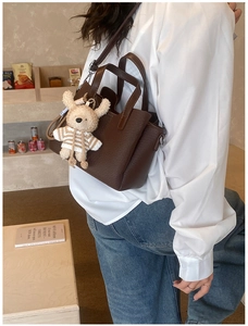 Detail of dark brown pebble leather tote bag with a white knit animal charm on a model