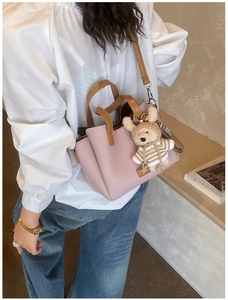 Detailed view of a pink pebbled leather handbag with brown handles and a cute bear charm