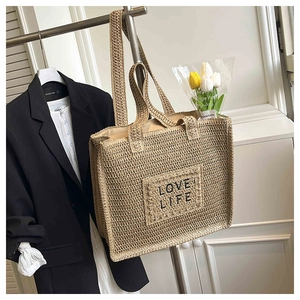 Gros plan détaillé du sac cabas en paille avec broderie noire LOVE LIFE sur le devant