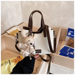Detail of color-block tote bag with plush bear charm and premium lychee texture