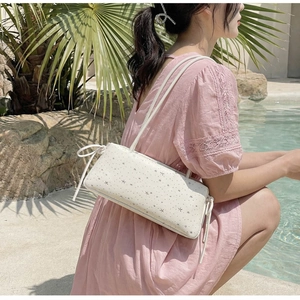 Sac baguette blanc à motif d'étoiles avec pompons montré dans un décor d'été au bord de l'eau