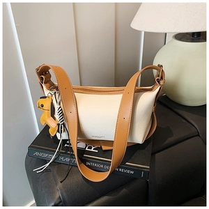 Détail du sac bandoulière crème en cuir avec bordure marron et breloque chien sur un livre