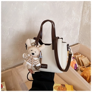Close-up of cream textured tote bag with dark brown handles and a plush rabbit charm