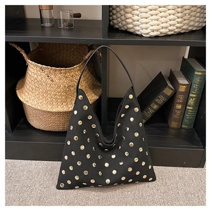 Macro shot of black suede tote bag featuring gold stud rivets on vintage wood shelf